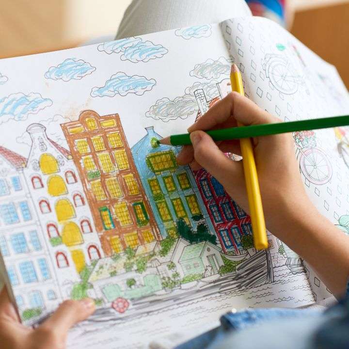 A person holding a sketch pad and coloring buildings with a beautiful scenery